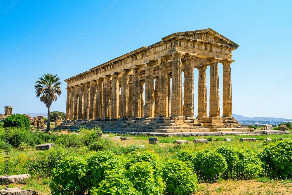 An ancient temple, adorned with intricate stone carvings and weathered columns, rises majestically against a clear blue sky, surrounded by lush vegetation that emphasizes its historical importance. An ancient temple, adorned with intricate stone carvings and weathered columns, rises majestically against a clear blue sky, surrounded by lush vegetation that emphasizes its historical importance.