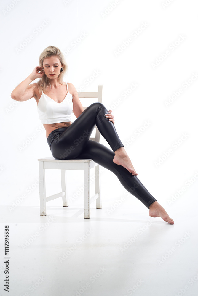 A blonde woman is wearing a white tank top and black pants. She is smiling and posing for the camera A blonde woman is wearing a white tank top and black pants. She is smiling and posing for the camera