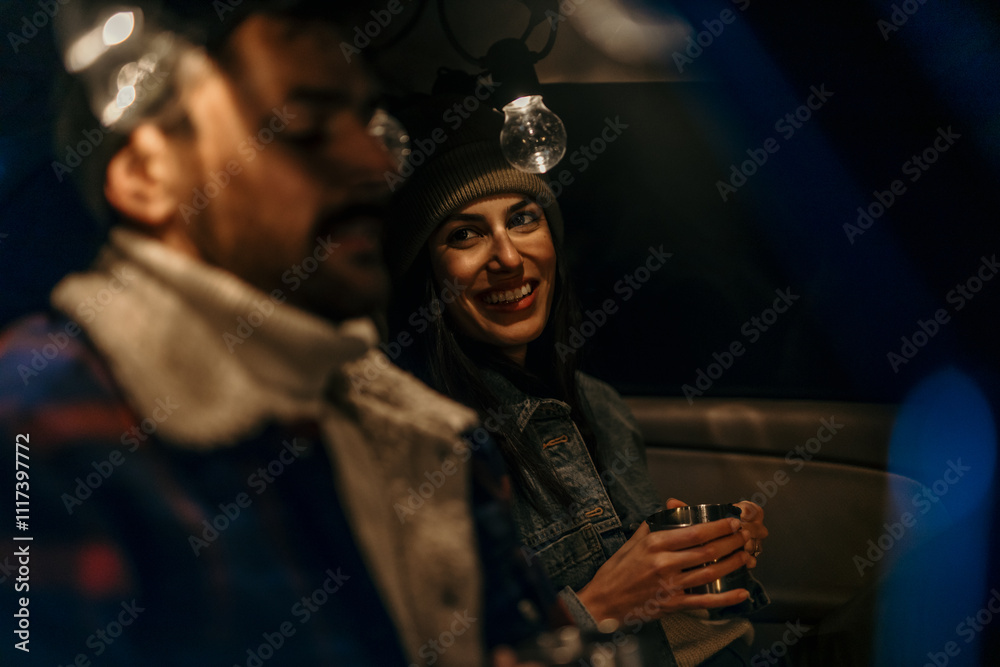 Man and woman enjoying warm drinks in the back of their truck on a cold night Man and woman enjoying warm drinks in the back of their truck on a cold night