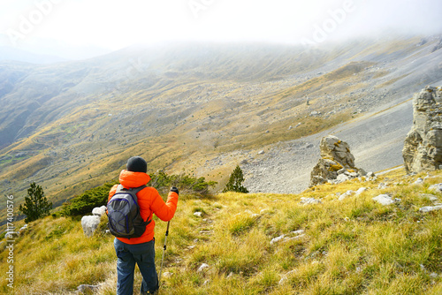 A traveler walks on a mountain path to a delightful mountain valley with low clouds hanging above it. A man who loves outdoor activities is hiking in the Komovi nature park on an autumn day. photo