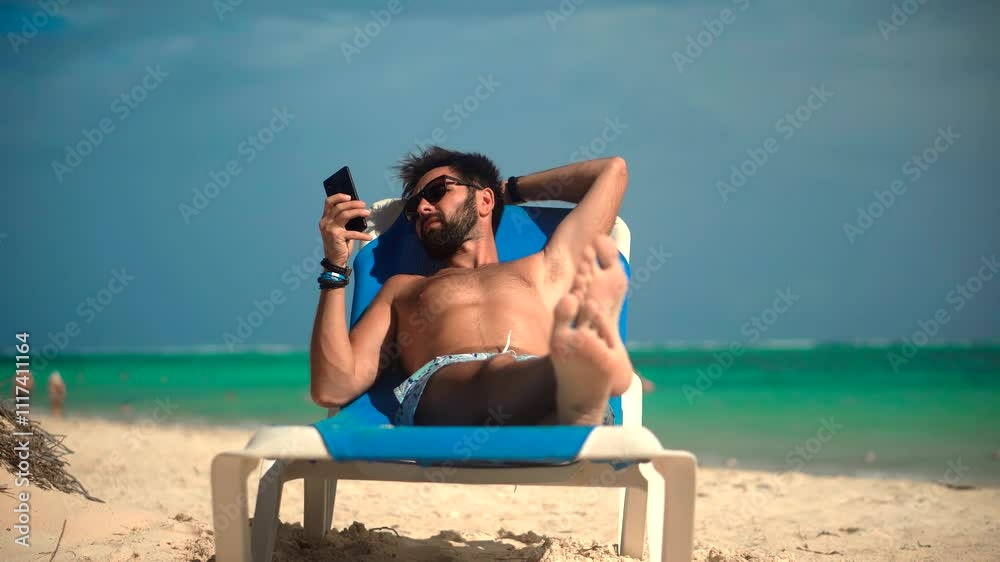 Relaxing man lounging on beach with smartphone and sunglasses Relaxing man lounging on beach with smartphone and sunglasses