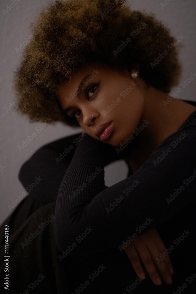 a close-up portrait of a person with curly hair, wearing a black top and an earring, in a dark and moody setting a close-up portrait of a person with curly hair, wearing a black top and an earring, in a dark and moody setting