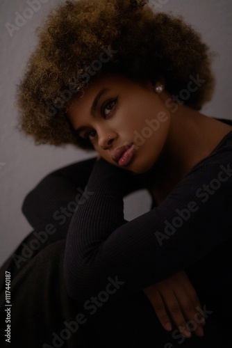 a close-up portrait of a person with curly hair, wearing a black top and an earring, in a dark and moody setting