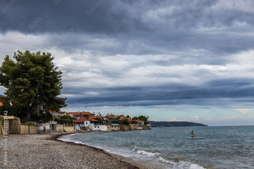 A serene coastal village with charming houses, a pebble beach, and dramatic clouds overhead. A paddle boarder adds a sense of adventure to the peaceful scene. A serene coastal village with charming houses, a pebble beach, and dramatic clouds overhead. A paddle boarder adds a sense of adventure to the peaceful scene.