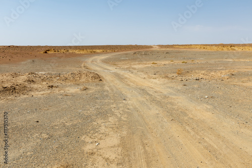 Dusty winding road through arid landscape under clear blue sky in remote area