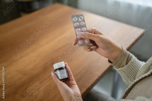 Woman hold pills and bottle at wooden table by the window