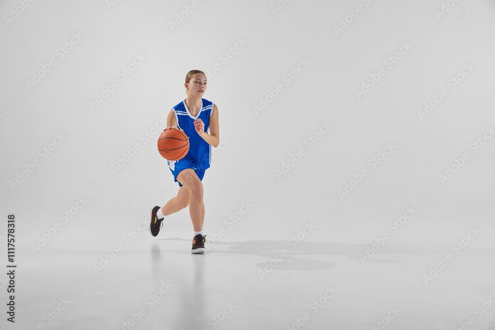 Full-length dynamic image of young teen girl, basketball player in blue uniform in motion with ball during game, training against white background. Concept of sport, youth, motion, healthy lifestyle Full-length dynamic image of young teen girl, basketball player in blue uniform in motion with ball during game, training against white background. Concept of sport, youth, motion, healthy lifestyle