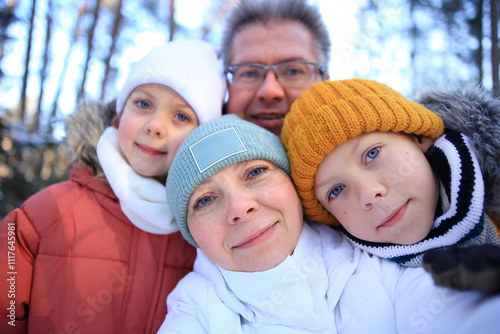 A cheerful mom, dad, daughter, and son pose together for a selfie in a picturesque winter landscape. Surrounded by snow covered trees and a serene snowy backdrop, their smiles radiate joy and