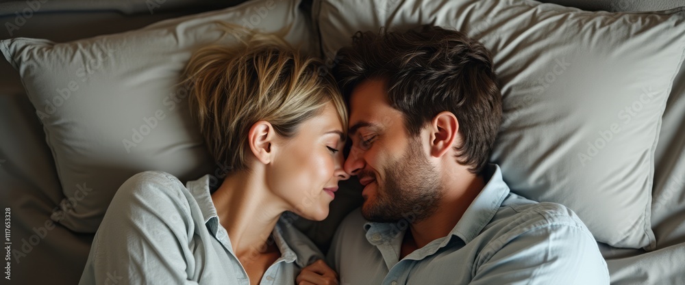 Obraz premium A tender moment unfolds as a couple lies closely together on a bed, their foreheads gently touching, radiating warmth and affection. The soft, muted colors of the bedding enhance the intimacy of the