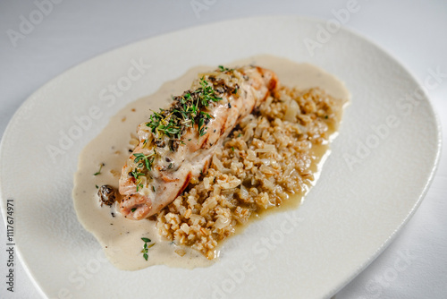 checken roll with mushroom white creamy sauce served on white plate and background, topped with herbs garnished with porridge