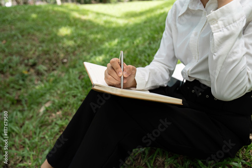 Person Reading and Working Outdoors in a Relaxed Natural Setting with Notebook and Pen photo