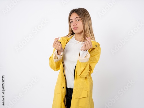 Beautiful teenager girl wearing yellow raincoat doing money gesture with hands, asking for salary payment, millionaire business