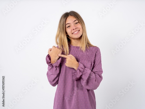 Beautiful teenager girl wearing purple T-shirt In hurry pointing to wrist watch, impatience, looking at the camera with relaxed expression photo