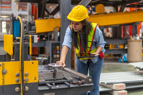 Female mechanical engineer in safety suit checking or inspecting a machine in metal sheet production system. Using technology for iron sheet formation and shape. Young factory worker examining machine