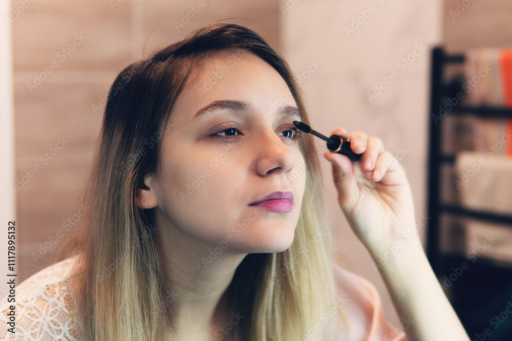 A woman applies mascara to her eyelashes in front of a mirror A woman applies mascara to her eyelashes in front of a mirror