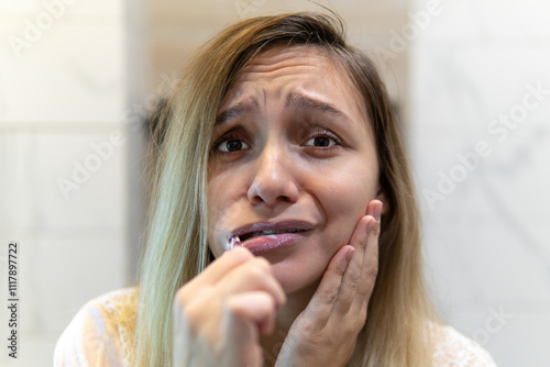 Canvas Print sad girl with a toothbrush in her mouth looks in the mirror