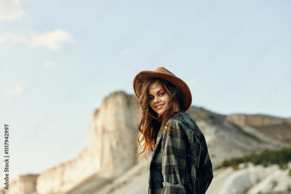 Woman in plaid shirt and hat standing in front of majestic mountain under clear blue sky Woman in plaid shirt and hat standing in front of majestic mountain under clear blue sky