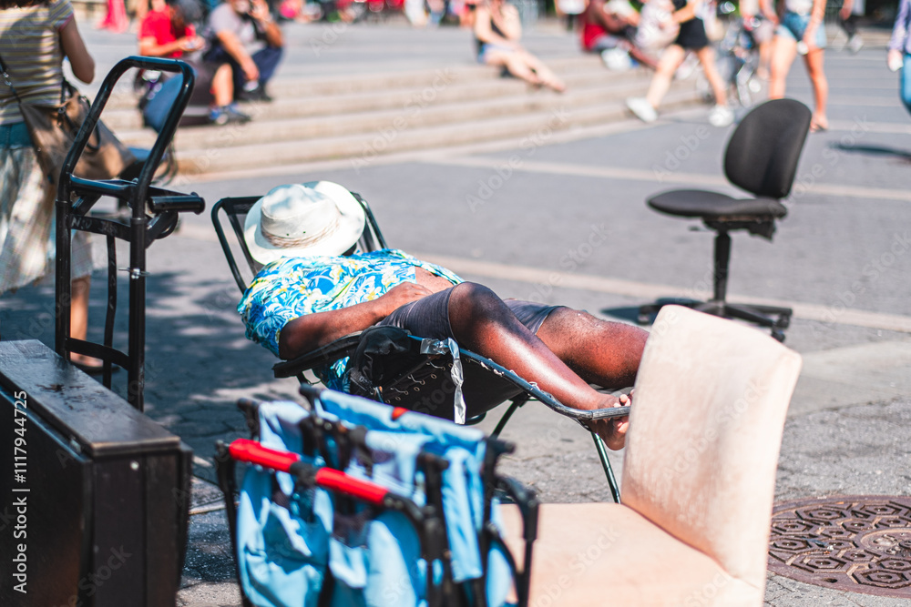 Obraz premium Man Relaxing in a Lounge Chair on a Sunny Day in a Busy Urban Park Scene Featuring People and Leisure Activities