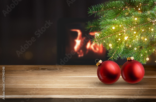 Empty wood table with red Christmas bauble, fir branch with bokeh light and warm fireplace glow in background. Festive winter holiday backdrop. Design for greeting card or template for product display