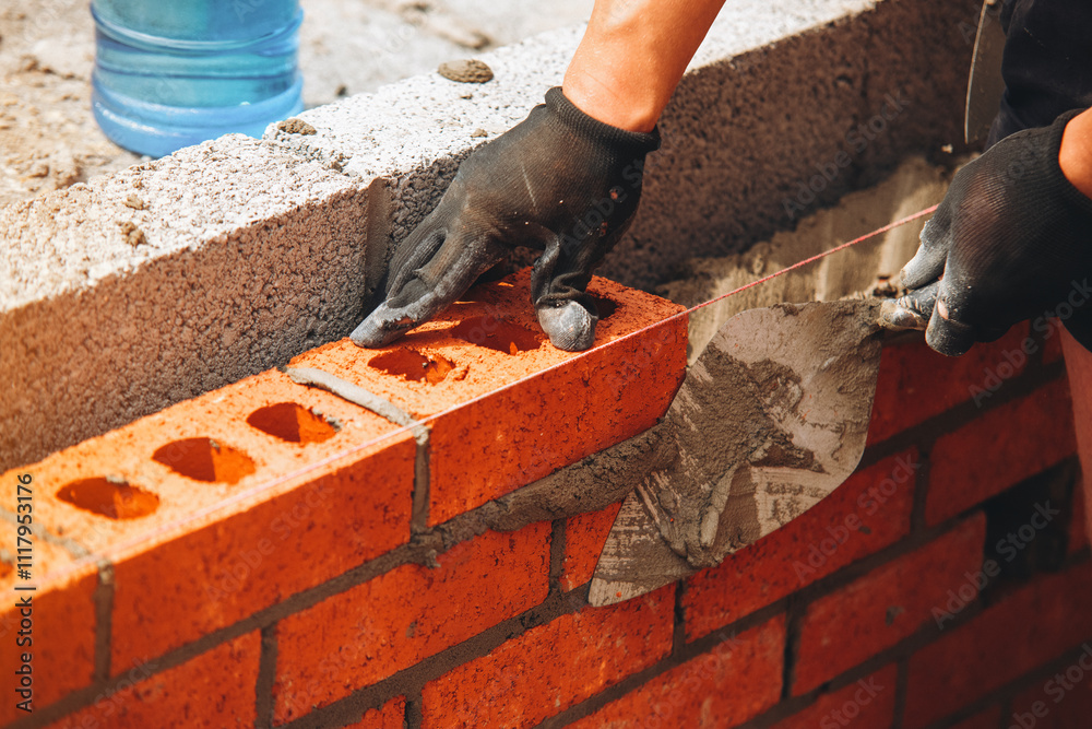 Craftsman bricklayer laying bricks with precision during construction at a building site in the afternoon sunlight Craftsman bricklayer laying bricks with precision during construction at a building site in the afternoon sunlight