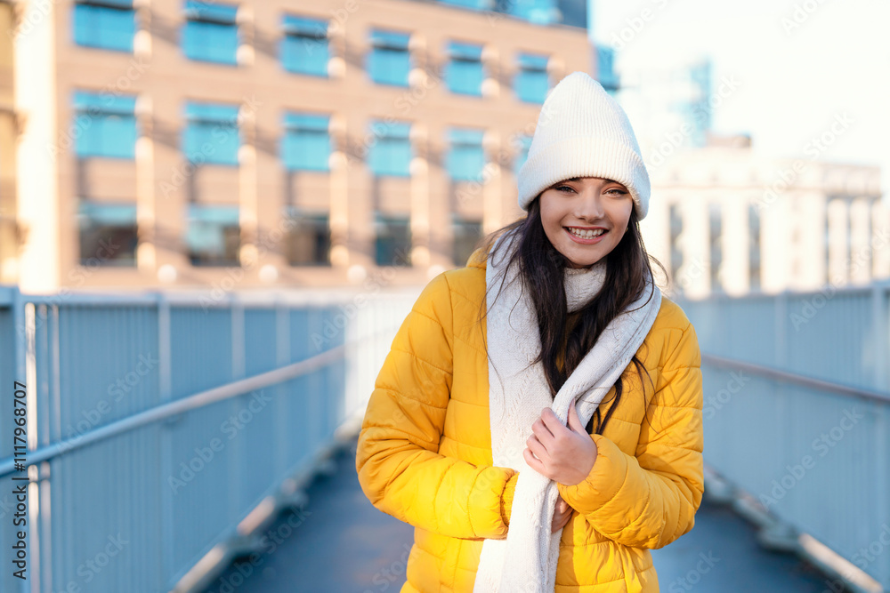 Smiling woman in yellow jacket and white beanie walks on urban bridge during winter morning Smiling woman in yellow jacket and white beanie walks on urban bridge during winter morning