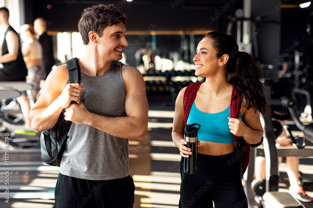 Man and woman athletes coming to morning sports training in modern gym, wearing backpacks and talking with each other Man and woman athletes coming to morning sports training in modern gym, wearing backpacks and talking with each other
