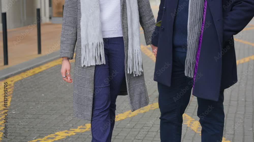 Stylish couple enjoys a walk while holding hands on a city street in chilly weather Stylish couple enjoys a walk while holding hands on a city street in chilly weather