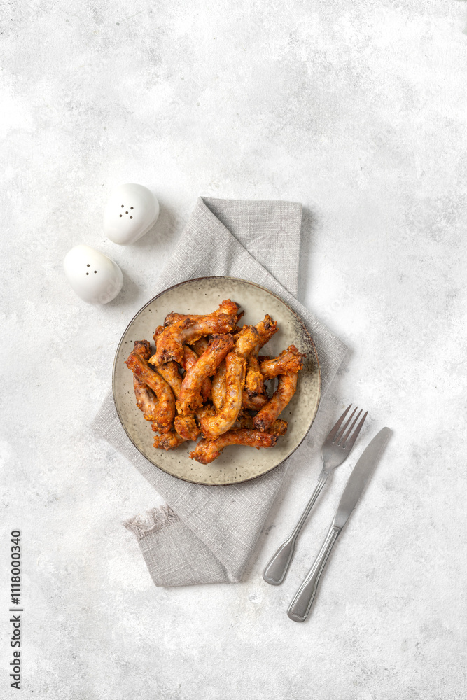 Baked chicken necks in a ceramic plate on a light culinary background top view