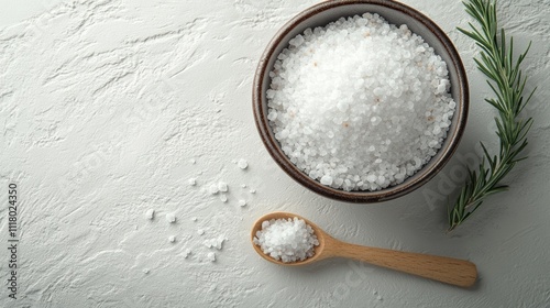 A bowl of sea salt and a small wooden spoon on a solid light blue background. Spa concept, exfoliation, skin care
