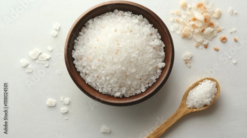 A bowl of sea salt and a small wooden spoon on a solid light blue background. Spa concept, exfoliation, skin care