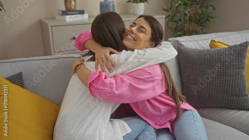 Two happy women embrace warmly on a cozy living room couch, showcasing their friendship or sisterly bond in a home setting adorned with vibrant cushions and indoor plants. photo