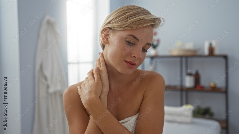 Obraz premium Woman relaxing in a serene spa environment with short blonde hair and a towel wrapped around her body, surrounded by wellness essentials on shelves in a softly lit interior space