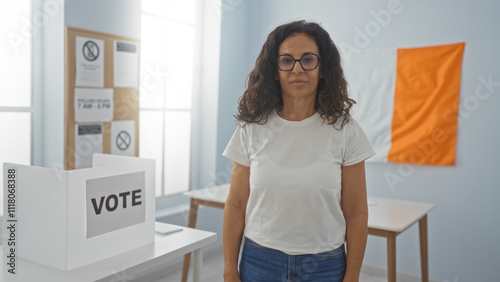 Woman standing in an irish electoral college room, with a voting booth, informational posters, and an irish flag in the background