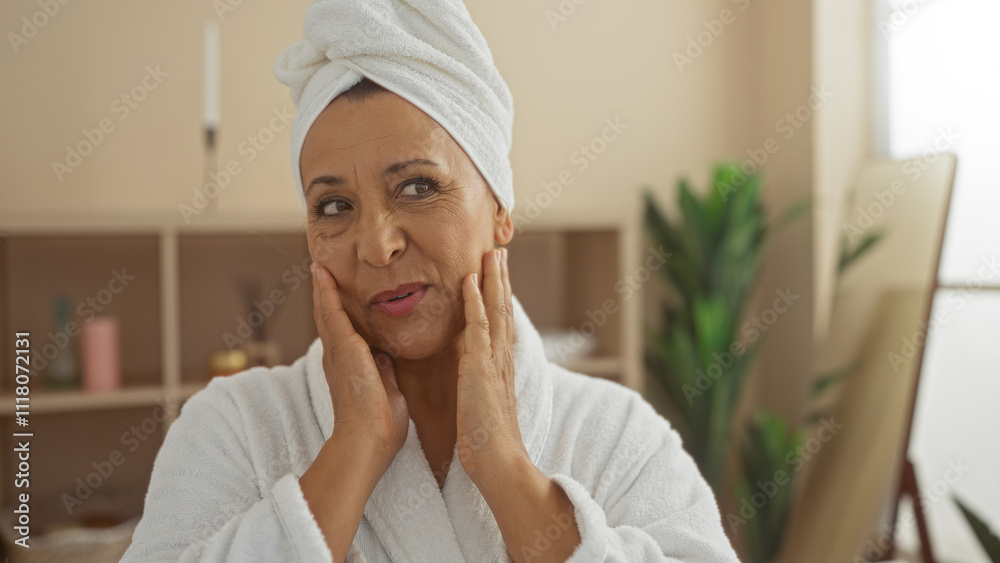 An elderly hispanic woman with a towel on her head and a bathrobe enjoys a moment of relaxation, touching her face in a spa room with a serene indoor setting. An elderly hispanic woman with a towel on her head and a bathrobe enjoys a moment of relaxation, touching her face in a spa room with a serene indoor setting.