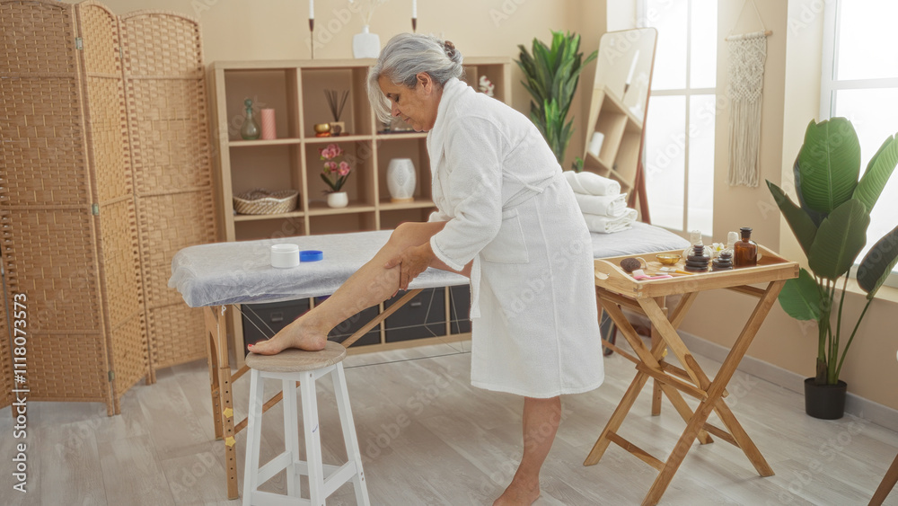 Elderly woman in a spa room applying lotion on her leg while wearing a white robe in a serene wellness setting with tropical plants and cozy furnishings Elderly woman in a spa room applying lotion on her leg while wearing a white robe in a serene wellness setting with tropical plants and cozy furnishings