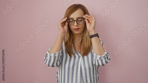 Middle-aged caucasian woman with glasses and striped shirt standing isolated against a pink background