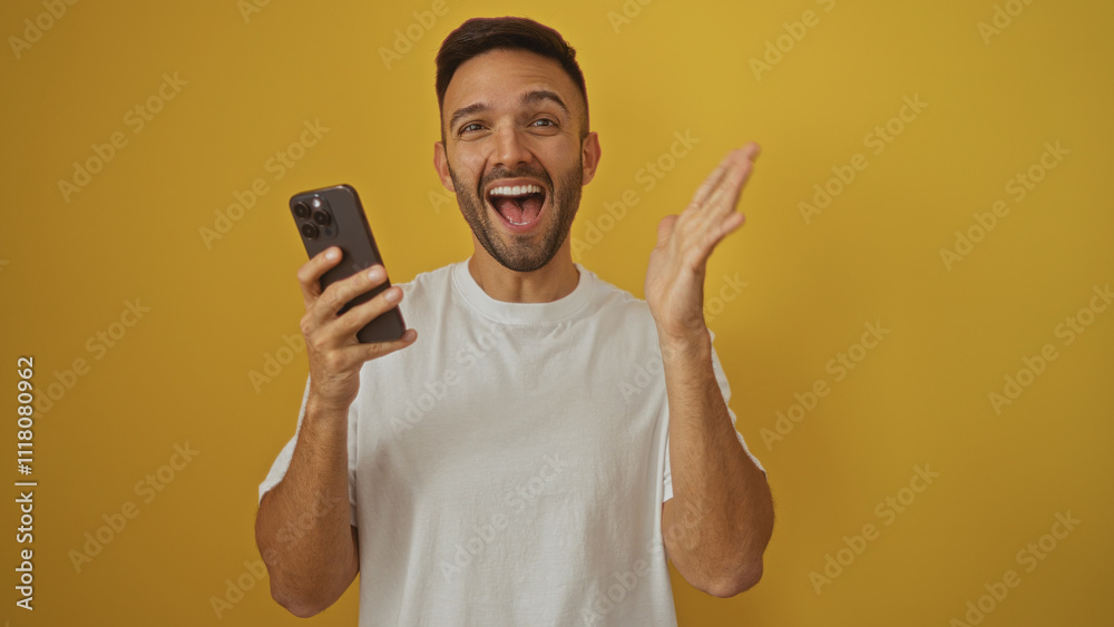 Handsome young hispanic man with a beard, smiling broadly and holding a smartphone, isolated against a vibrant yellow background. Handsome young hispanic man with a beard, smiling broadly and holding a smartphone, isolated against a vibrant yellow background.