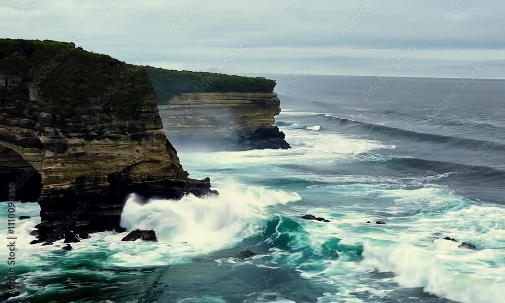 The rugged rocks of the beach meet the turbulent sea as the waves crash and foam at the bottom.