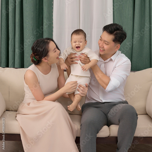 Young parents are playing with their 10 -month -old son on the sofa, Green curtain at the back photo