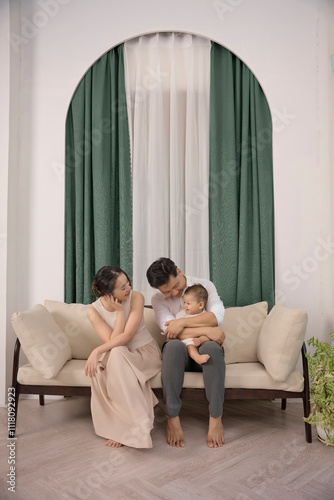 Young parents are playing with their 10 -month -old son on the sofa, Green curtain at the back photo