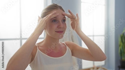 Young woman touching her face in a spa with indoor lighting, appearing focused and relaxed in a beauty treatment room