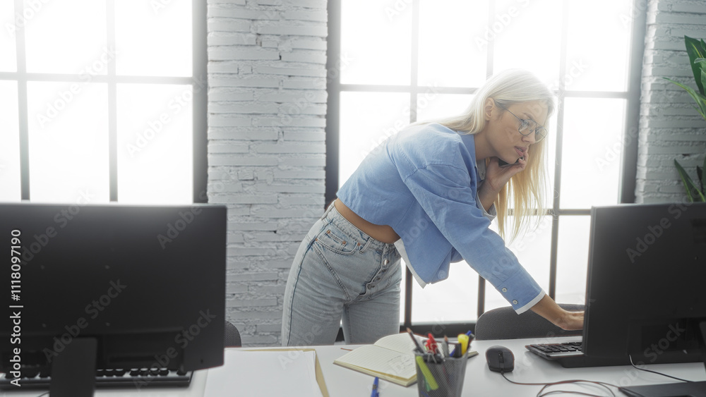 Woman talking on phone in modern office setting with computer desk and large window showcasing professional indoor workspace atmosphere. Woman talking on phone in modern office setting with computer desk and large window showcasing professional indoor workspace atmosphere.