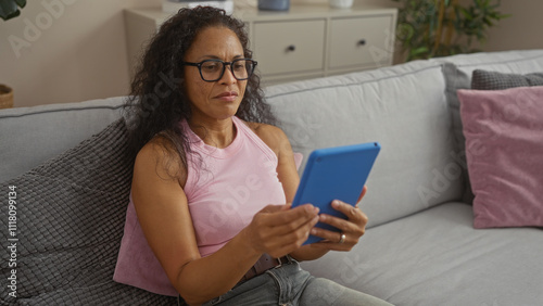 Woman using tablet sitting on sofa in cozy living room with plants and cushions, portraying a homely and relaxed atmosphere