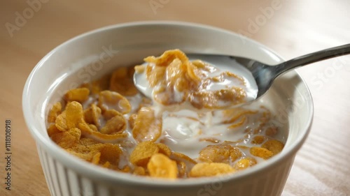slow motion scooping cornflakes cereal with a spoon from a bowl full of milk