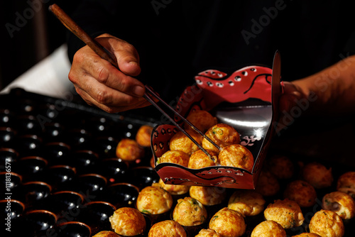 Fototapeta Naklejka Na Ścianę i Meble -  A vendor skillfully serves Japanese Takoyaki using chopsticks