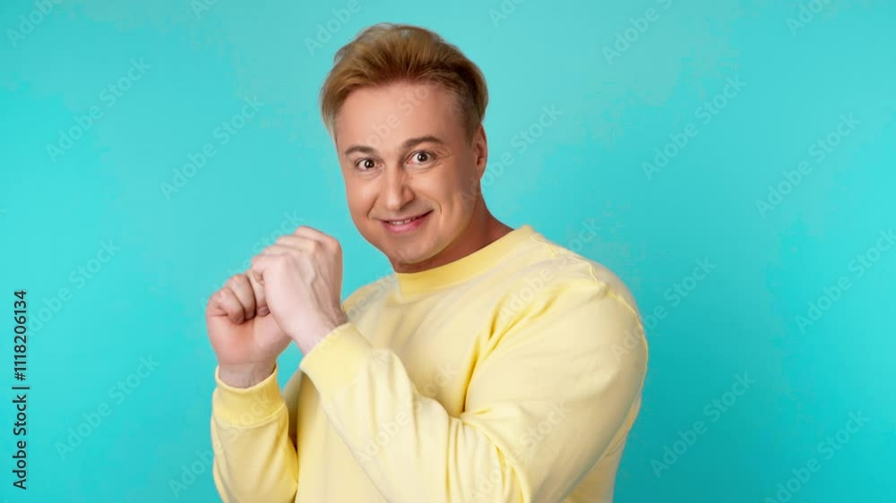 Positive man dancing having fun rhythm to music, enjoying life, entertainment. Carefree guy excited dance in a yellow sweatshirt. Studio shot isolated on blue background. Positive man dancing having fun rhythm to music, enjoying life, entertainment. Carefree guy excited dance in a yellow sweatshirt. Studio shot isolated on blue background.