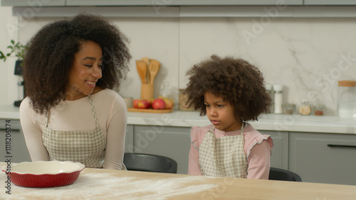 African American family custody adopted child smiling mother woman mom talking to sad upset frown shy little kid daughter offended girl at kitchen table teaching cooking baking flour cook talk problem