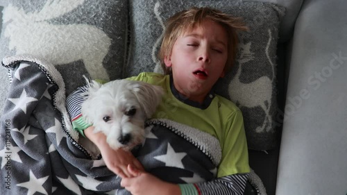 Sick child, preschool boy, lying in bed with a fever, resting at home with his pet dog, mom checking on him