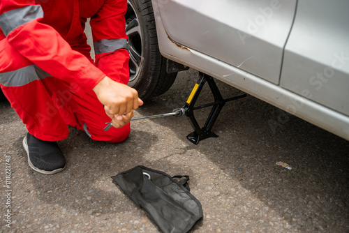 Wallpaper Mural A mechanic using a jack to change a tire on a silver vehicle in an outdoor setting. Torontodigital.ca