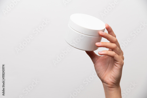 Close-up of a woman's hand holding a white jar of cream, mockup for advertising. Girl on a white background showing a cosmetic product